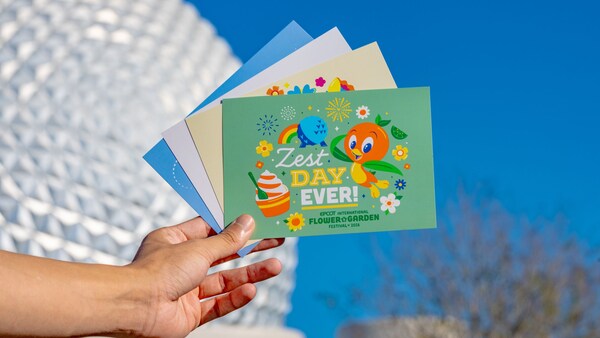 A hand holding 4 cards fanned out with the top card displaying the words ‘Zest Day Ever’ and artwork for the Epcot International Flower & Garden Festival 2026