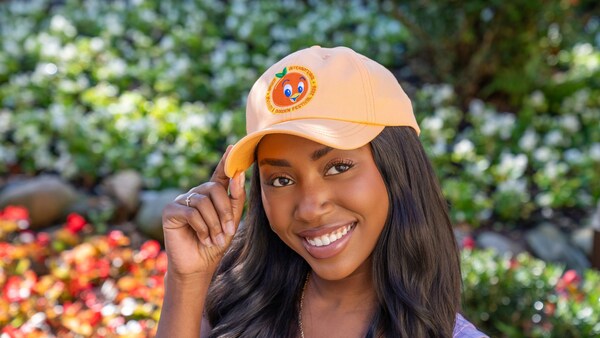 A woman wearing a baseball hat featuring the Epcot International Flower & Garden Festival 2026