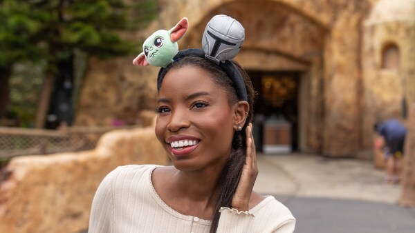 A Guest wearing a Star Wars themed Mickey Mouse ear headband while smiling near Tatooine Traders at Disney's Hollywood Studios theme park