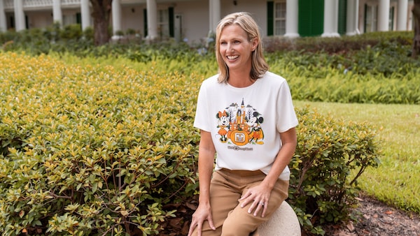 A Guest wearing a Walt Disney World Halloween themed T shirt sits near landscaped greenery
