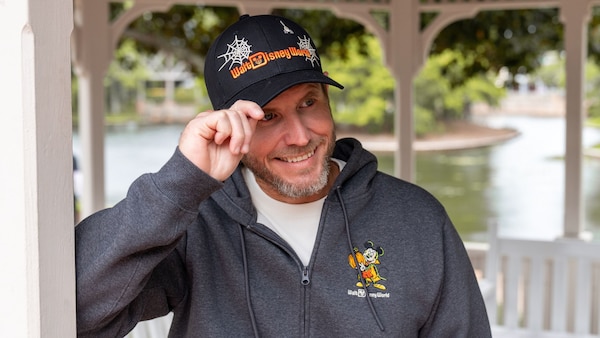 A Guest wearing a Halloween themed Walt Disney World hoodie and cap inside a waterfront gazebo