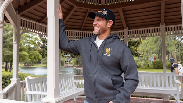 A Guest wearing a Halloween themed Walt Disney World hoodie and cap inside a waterfront gazebo