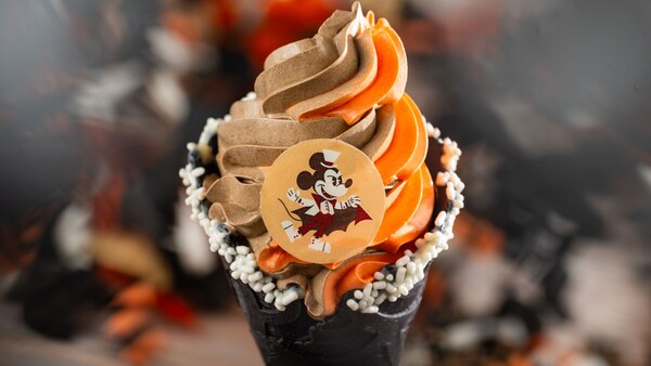 A Vampire Mickey Cone with pumpkin and chocolate soft serve swirl, topped with sprinkles and a chocolate Mickey Mouse coin