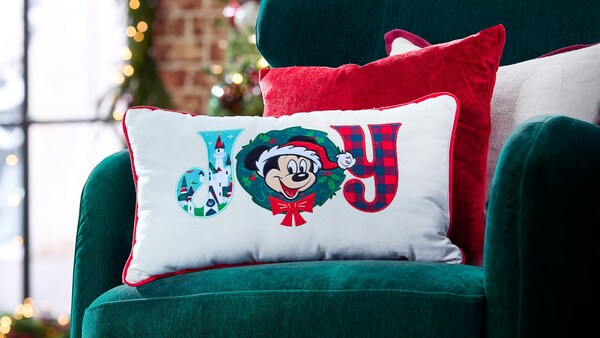 Un cojín decorativo con temática de Navidad en el que aparece Mickey Mouse y la palabra “Joy”