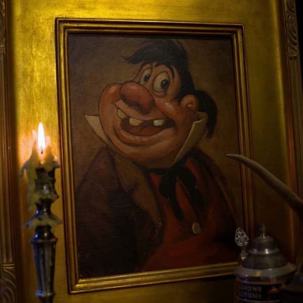 Candles and books surround a gold framed image of Beauty and the Beast's LeFou character