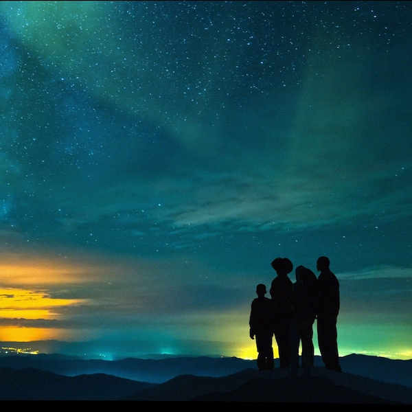 Family stands on a mountain looking at a beautiful blue and yellow night sky