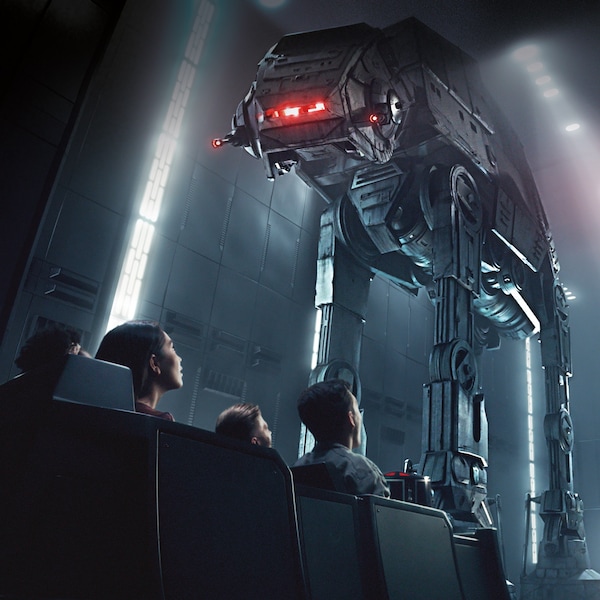 People in a transport vehicle inside a hanger bay look up at 2 towering AT-AT walkers