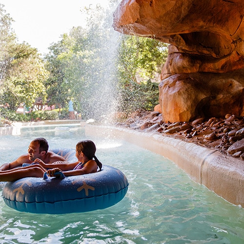 Three Guests riding inner tubes through a gentle waterfall at Cross Country Creek in Disney’s Blizzard Beach water park