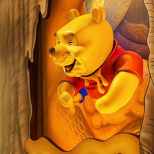 Winnie the Pooh covered in honey peeking out of a tree at The Many Adventures of Winnie the Pooh
