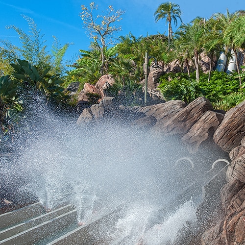A boat sitting next to rocks and greenery above water splashing out from waterslides