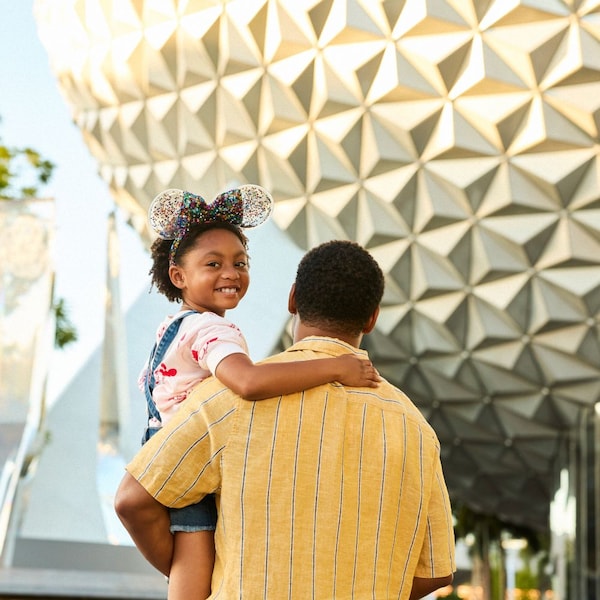 A father holding his smiling young daughter in his arms as he walks towards Spaceship Earth at Epcot