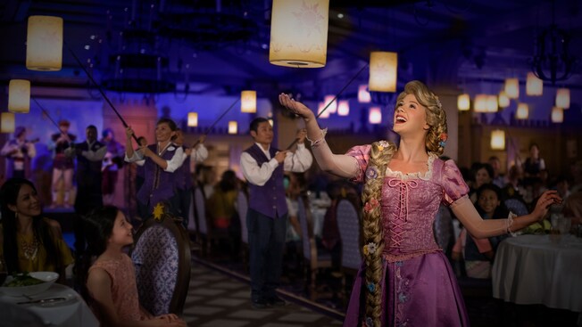 In a dinner show, Rapunzel admires a hanging lantern while Guests and musicians look on