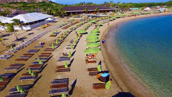 Un club de playa frente al mar con camastros, sombrillas y una gran carpa