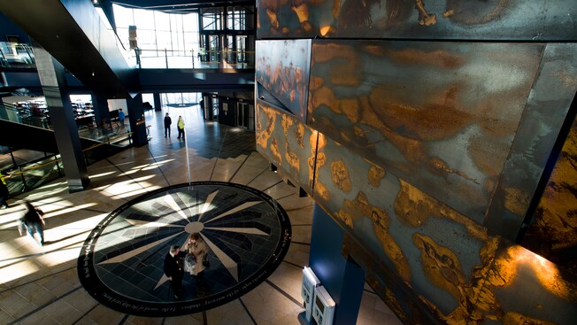The spacious atrium of Titanic Belfast reveals multiple floors, escalators and a mosaic of a compass on the floor