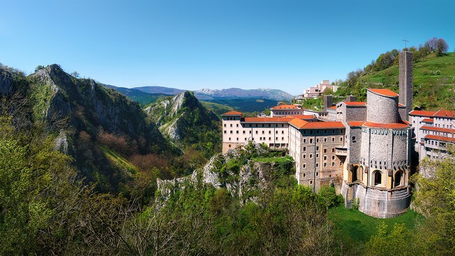 A large multi story sanctuary with a bell tower built into the edge of a mountain