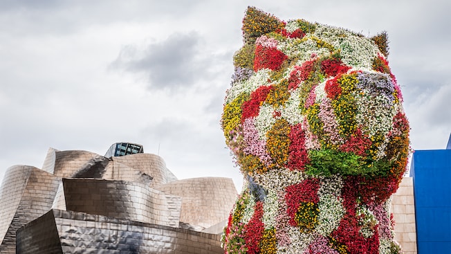 Uma escultura de flores monumental de um filhote de cachorro que fica do lado de fora da arquitetura curvilínea do Museu Guggenheim em Bilboa, Espanha Uma escultura de flores monumental de um filhote de cachorro que fica do lado de fora da arquitetura curvilínea do Museu Guggenheim em Bilboa, Espanha