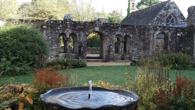 A medieval stone church and arcade in a garden with a fountain