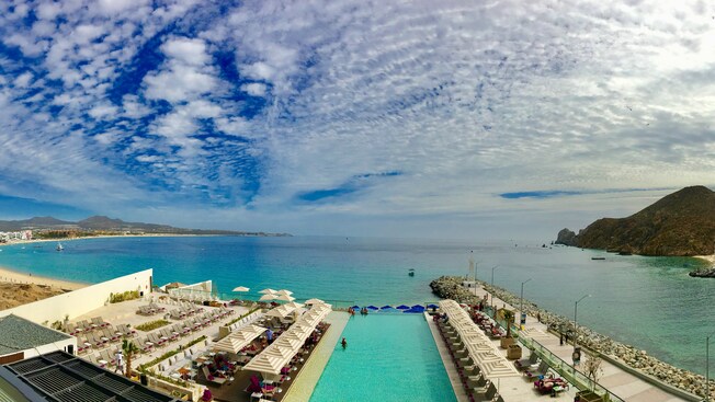 Beach chairs and umbrellas surrounding an infinity pool next to a tranquil seashore