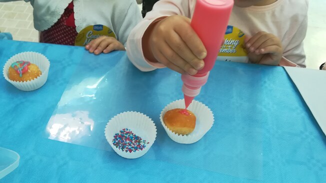 2 people decorate cupcakes with sprinkles and a glaze
