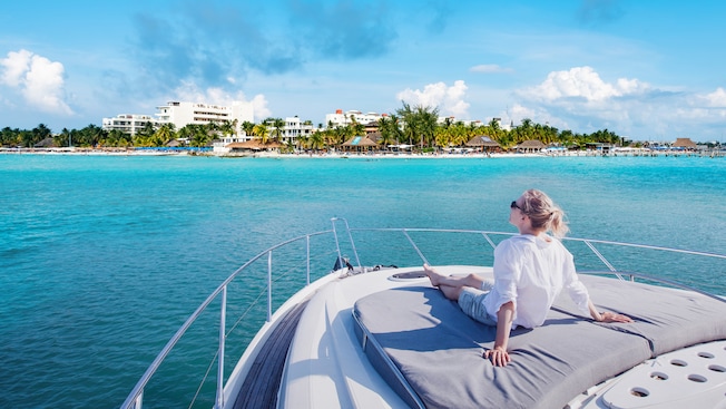 A woman relaxing on the sundeck of a boat while looking out to a tropical beach filled with palm trees and resorts A woman relaxing on the sundeck of a boat while looking out to a tropical beach filled with palm trees and resorts