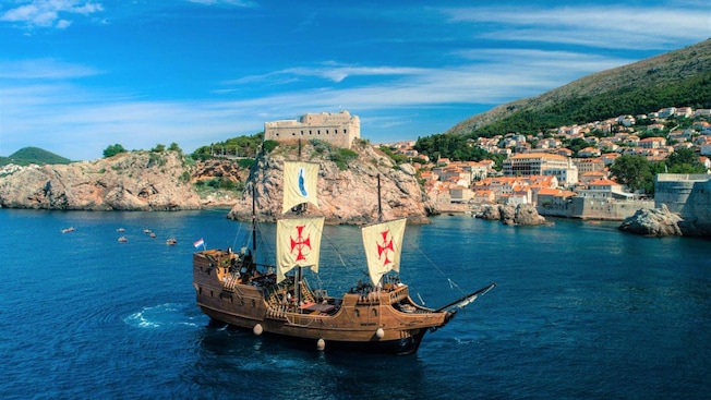 An antique galleon ship sailing next to the medieval town of Dubrovnik