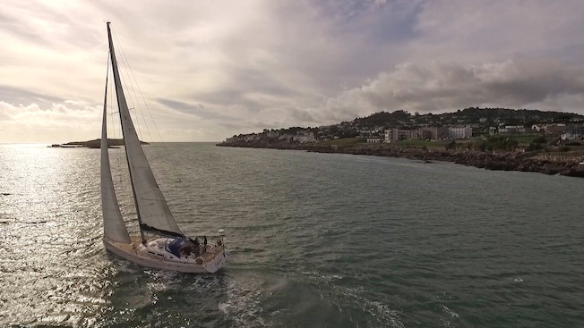A sailing yacht gliding on the water near a shore occupied with buildings A sailing yacht gliding on the water near a shore occupied with buildings