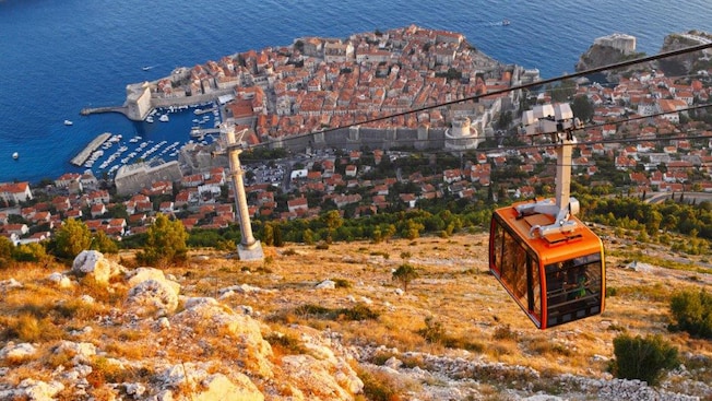 A cable car traveling up a steep mountain near a medieval town and coastline A cable car traveling up a steep mountain near a medieval town and coastline
