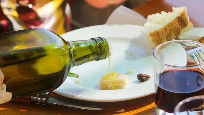 Aceite de oliva que sale de una botella sobre un trozo de queso junto a un poco de pan y una copa de vino Aceite de oliva que sale de una botella sobre un trozo de queso junto a un poco de pan y una copa de vino