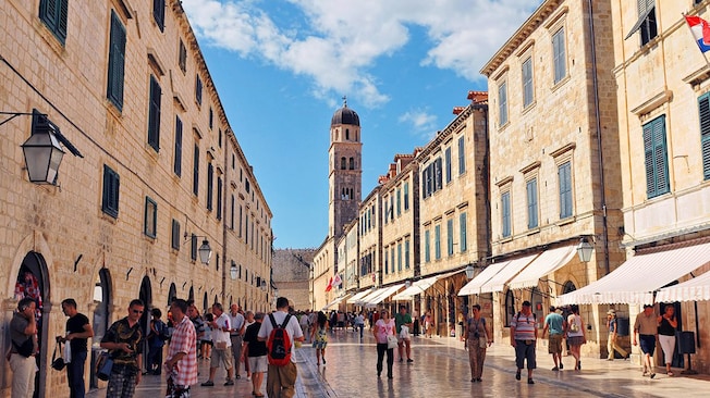 People walking on a pedestrian street in a medieval town lined with shops and a bell tower People walking on a pedestrian street in a medieval town lined with shops and a bell tower