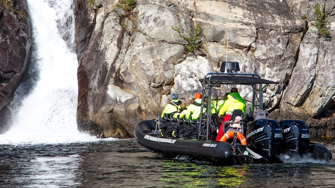 A rigid inflatable boat filled with passengers navigating toward a waterfall A rigid inflatable boat filled with passengers navigating toward a waterfall
