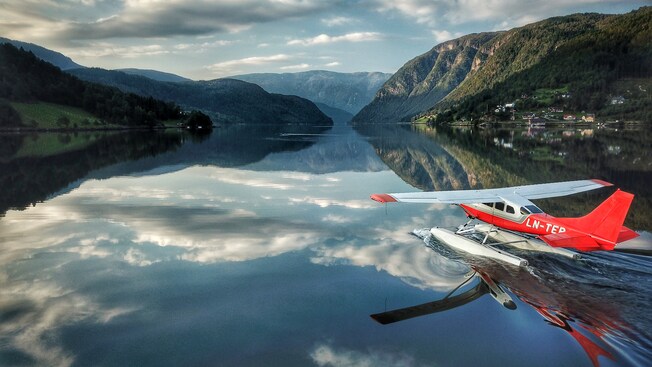 A seaplane landing on a tranquil lake surrounded by mountains