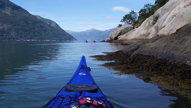 La parte frontal de un kayak deslizándose por las aguas de un fjord hacia otros dos personas que practican kayak La parte frontal de un kayak deslizándose por las aguas de un fjord hacia otros dos personas que practican kayak