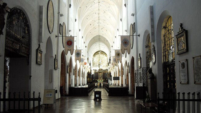 The interior of a historical church with a high ceiling, stone floor, wooden pews and cast iron detailing