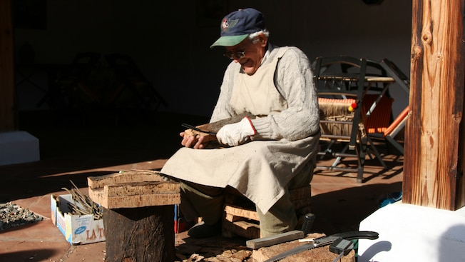 A man sitting on a stump while stripping bark from blocks of cork A man sitting on a stump while stripping bark from blocks of cork