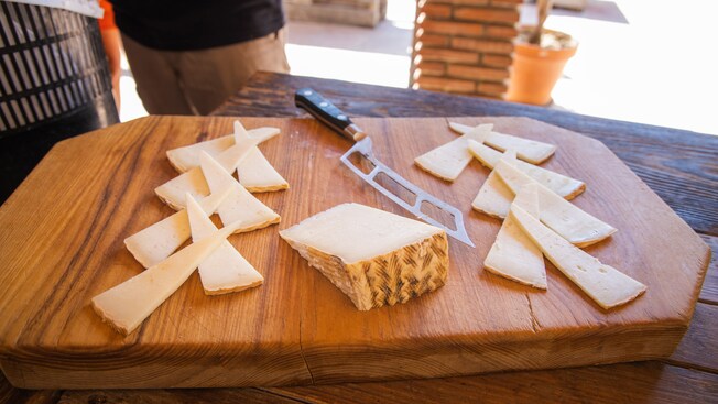A wooden cutting board with a knife and slices of hard cheese