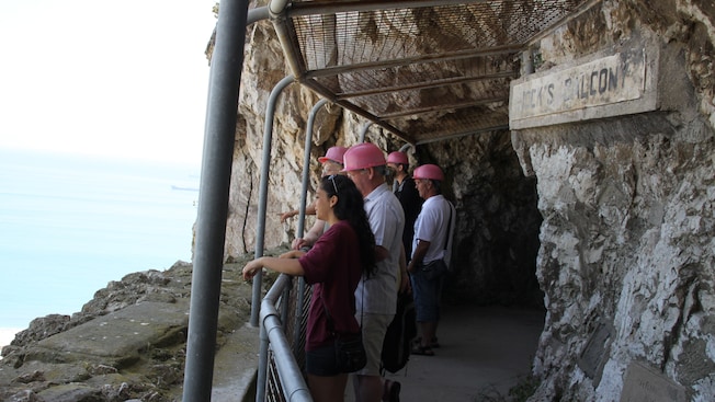 A group of people in hard hats standing outside a mountain cave looking out to the sea A group of people in hard hats standing outside a mountain cave looking out to the sea