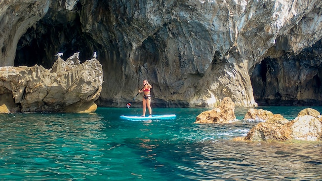 A woman standing on a paddleboard near a coastal cave A woman standing on a paddleboard near a coastal cave