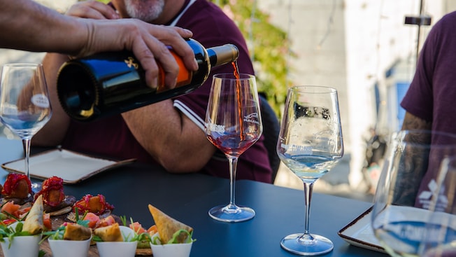 Uma mão derramando vinho em um copo ao lado de uma bandeja de tapas Uma mão derramando vinho em um copo ao lado de uma bandeja de tapas