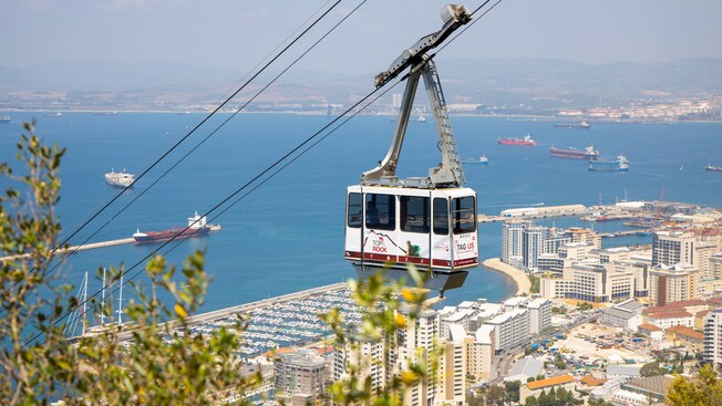An aerial tram ascending a mountain above a coastal city