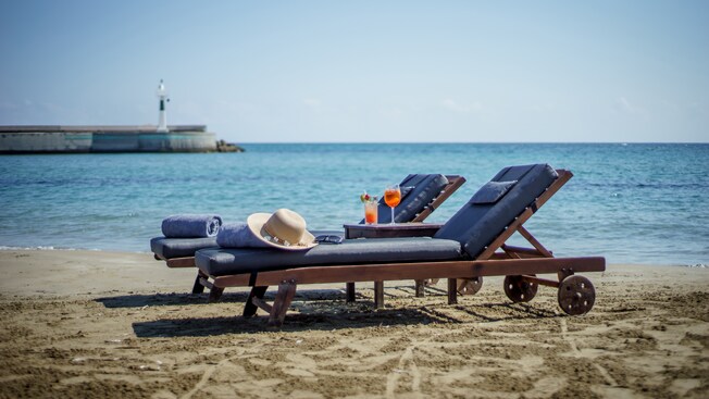 A beachside setup consisting of 2 sunbeds, towels, a hat and a small table with 2 beverages A beachside setup consisting of 2 sunbeds, towels, a hat and a small table with 2 beverages
