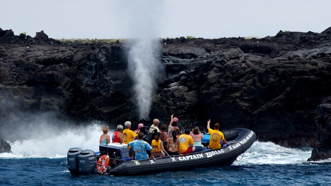 An inflatable speedboat filled with passengers sailing close to a blow hole