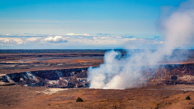 Steam comes from a large hole in the earth in a large dirt field