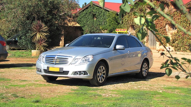 A sedan with a sign on the roof that says TAXI is parked in the grass in front of a building A sedan with a sign on the roof that says TAXI is parked in the grass in front of a building