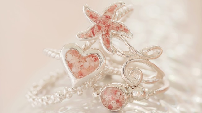 3 jewlery rings with centers styled into a star fish, heart and circle, all staged on a textured surface 3 jewlery rings with centers styled into a star fish, heart and circle, all staged on a textured surface
