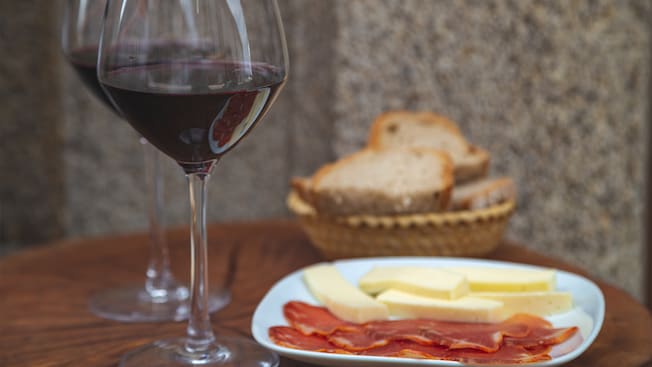 Um copo de vinho ao lado de uma cesta de pão e um prato de presunto e queijo Um copo de vinho ao lado de uma cesta de pão e um prato de presunto e queijo