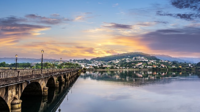 A stone Rennaissance era bridge leading to a coastal town with twinkling lights A stone Rennaissance era bridge leading to a coastal town with twinkling lights
