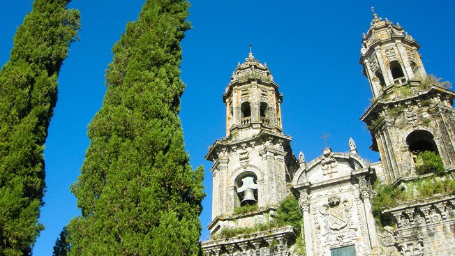 2 ciprestes ao lado dos campanários ornamentados de uma igreja gótica