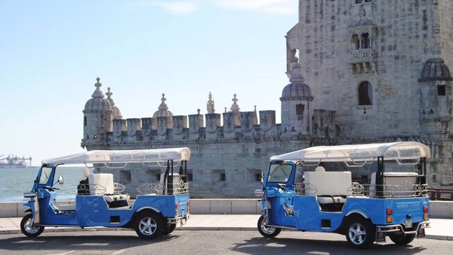 Two 3-wheeled motorized vehicles parked outside a historical building by the sea