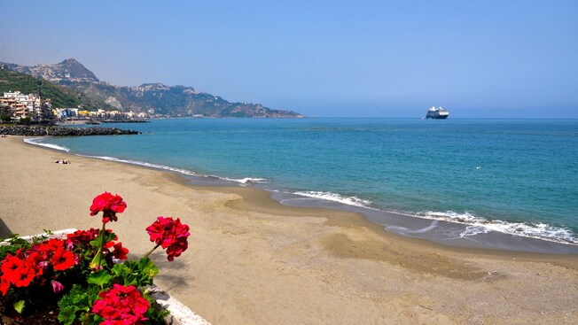 Las flores en una maceta se asoman a una extensa costa en el pueblo costero de Giardini Naxos