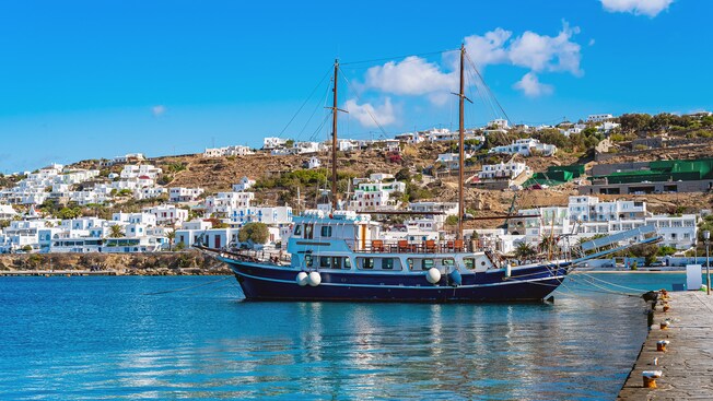 Un barco griego tradicional anclado junto al mar junto a pueblo escarpado